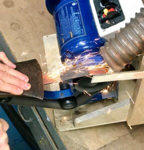 Axe being sharpened on a belt sander creating lots of sparks