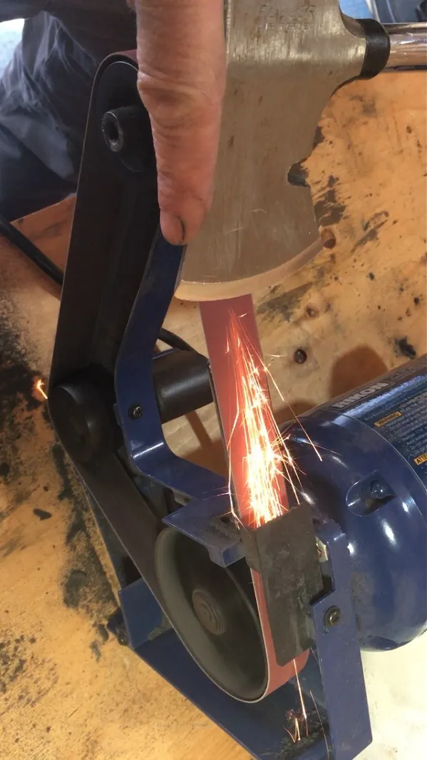 axe being sharpened on a belt grinder in Halifax, with sparks flying off it
