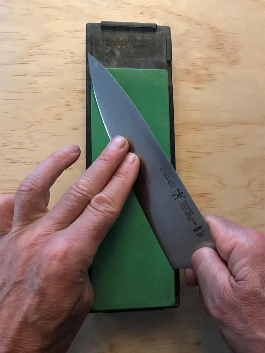 Man's hands sharpening a chef knife on a green Japanese waterstone
