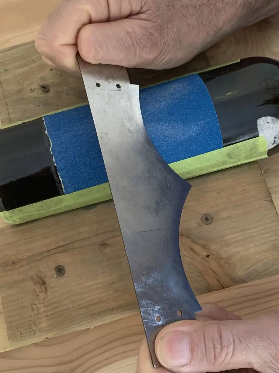 Man sharpening a custom blade with two rounded blades on a custom set up with blue sandpaper